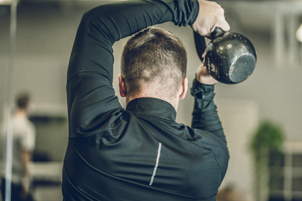 Guy holding kettle bell doing halo for shoulders